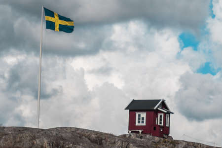 A classic red hut in Sweden next to a Swedish flagの写真素材