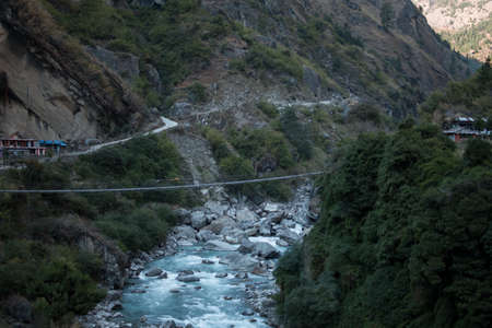 Nepalese mountain village by a suspension bridge over the Marshyangdi river gorge valley, Annapurna...