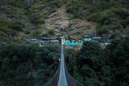 Nepalese mountain village by a suspension bridge over the Marshyangdi river gorge valley, Annapurna...