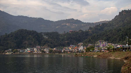 View over a part of Pokhara with colorful bouildings and paris wheel with the mountains in the background by the lakeside in Nepalのeditorial素材