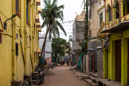 Puri, India - February 3, 2020: A few unidentified people walks on a small local dirt road with a yellow building and parked motorbikes on February 3, 2020 in Puri, Indiaのeditorial素材