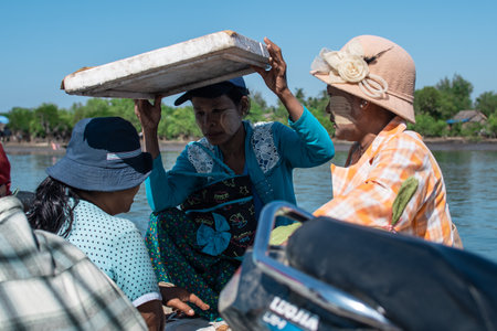 Chaung Thar, Myanmar - December 26, 2019: Portrait of three unidentified women with thanaka on their faces, one holds styrofoam for shade on December 26, 2019 in Chaung Thar, Myanmarのeditorial素材