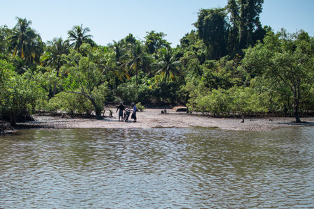 Ngwesaung, Myanmar - December 26, 2019: Two unidentified local people with a motorbike by mangrove and palm trees during low tide on December 26, 2019 in Ngwesaung, Myanmarのeditorial素材