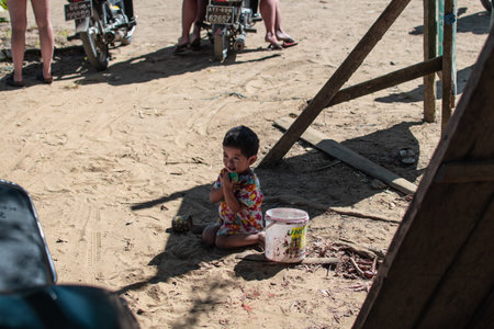 Ngwesaung, Myanmar - December 26, 2019: A young burmese child in a colorful dress sits in the sand...