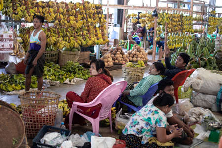 YANGON, MYANMAR - DECEMEBER 31 2019: Local burmese people attending a street market by plenty of bananas and coconutsのeditorial素材