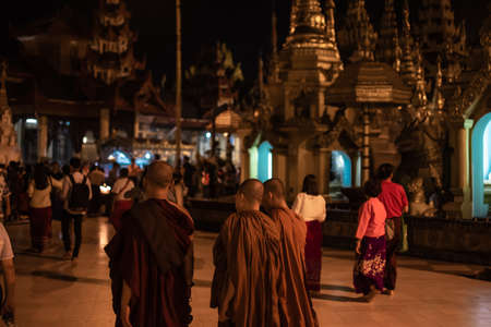 Yangon, Myanmar - December 30, 2019: Three monks walks around the Shwedagon Pagoda and its...