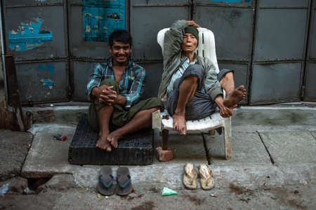 Yangon, Myanmar - December 30, 2019: Portrait of two local burmese people sitting on the side of the roadのeditorial素材