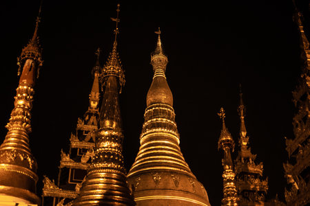 Yangon, Myanmar - December 30, 2019: The top of several shiny golden pagodas against the dark night sky at the Shwedagon Pagodaのeditorial素材