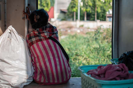 YANGON, MYANMAR - DECEMEBER 31 2019: A local burmese woman in a red andpink striped hoodie sits in...