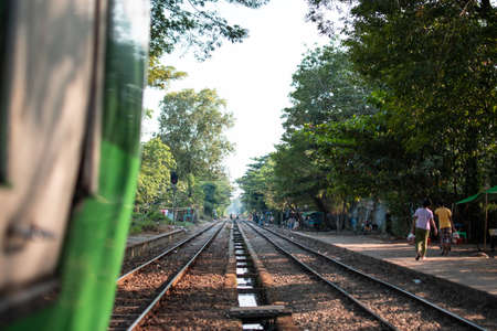 YANGON, MYANMAR - DECEMEBER 31 2019: The traditional circle train passing through a local platform stop with view over burmese people walking pastのeditorial素材