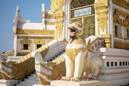 YANGON, MYANMAR - JANUARY 1 2020: Sunlight hits a decorated lion statue outside white and golden Swe Taw Myat Pagodaのeditorial素材