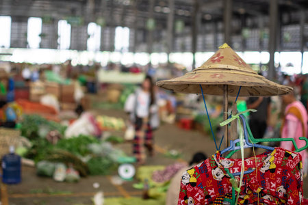 A simple hat and a decorativered dress hanging on a stick at a local fruit and vegetables market in rural Myanmarの写真素材