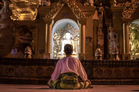 Yangon, Myanmar - December 30, 2019: A woman prays and meditates, sitting in front of a buddha statue at the Shwedagon Pagodaのeditorial素材