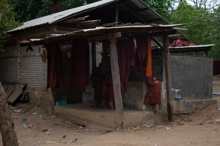 BAGAN, NYAUNG-U, MYANMAR - 2 JANUARY 2020: A few young monks stands by a water supply well by a house where red buddhist robes hang driesのeditorial素材