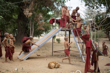BAGAN, NYAUNG-U, MYANMAR - 2 JANUARY 2020: Young monks plays, runs, jumps, climbs, laughs and have fun together at a local playground with a slideのeditorial素材