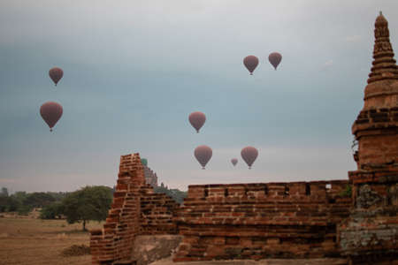 BAGAN, NYAUNG-U, MYANMAR - 2 JANUARY 2020: A few hot air balloons rises above a historic pagoda temple in the distanceのeditorial素材