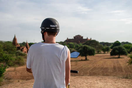 BAGAN, NYAUNG-U, MYANMAR - 3 JANUARY 2020: A male tourist on an electric bike on top of a hill looking out over fields and historical templesのeditorial素材