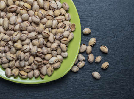 Pistachio nuts in a green plate on a dark backgroundの写真素材