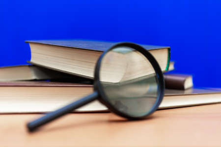 Selective focus Magnifying glass a few closed books on a brown wooden table blue backgroundの写真素材