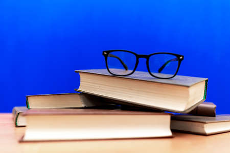 Books and eyeglasses on a wooden table, on blue trendy soft background