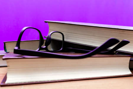 Books and eyeglasses on a wooden table, on purple trendy soft backgroundの写真素材