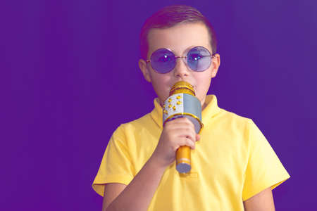 Close up image.The young boy kid child 9s old in yellow t shirt and blue eyeglasses is singing music on purple foggy toned illuminated stage.の写真素材