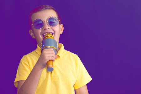 Close up image.The young boy kid child 9s old in yellow t shirt and blue eyeglasses is singing music on purple foggy toned illuminated stage.の写真素材