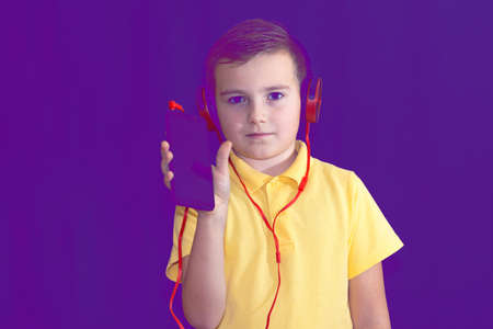 Close up of one young school boy using his phone and listening music alone or watching videos.Purple foggy toned background.の写真素材