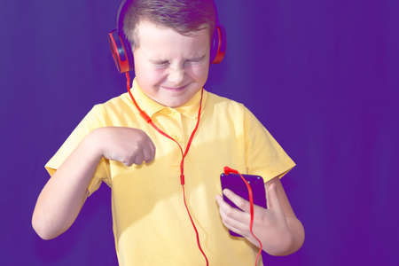 Close up of closed eyes young school boy using his phone and listening music alone or watching videos.Purple foggy toned background.の写真素材