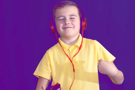 Close up of closed eyes young school boy using his phone and listening music alone or watching videos.Purple foggy toned background.の写真素材