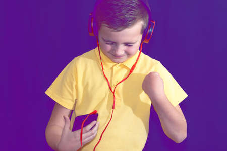 Close up of closed eyes young school boy using his phone and listening music alone or watching videos.Purple foggy toned background.の写真素材
