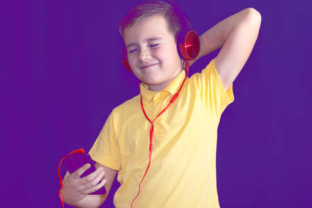 Close up of closed eyes young school boy using his phone and listening music alone or watching videos.Purple foggy toned background.の写真素材