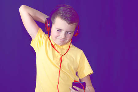 Close up of closed eyes young school boy using his phone and listening music alone or watching videos.Purple foggy toned background.の写真素材