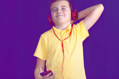 Close up of closed eyes young school boy using his phone and listening music alone or watching videos.Purple foggy toned background.の写真素材