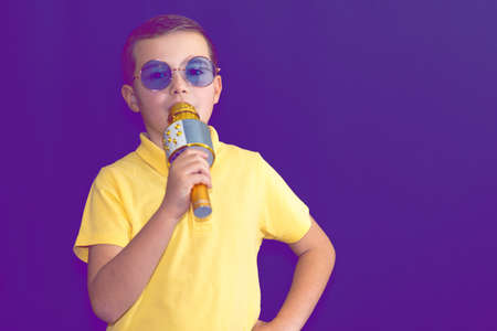 Close up image.The young boy kid child 9s old in yellow t shirt and blue eyeglasses is singing music on purple foggy toned illuminated stage.の写真素材