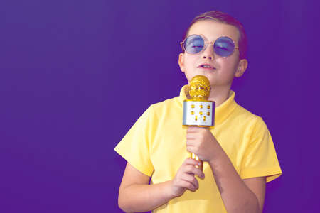 Close up image.The young boy kid child 9s old in yellow t shirt and blue eyeglasses is singing music on purple foggy toned illuminated stage.の写真素材