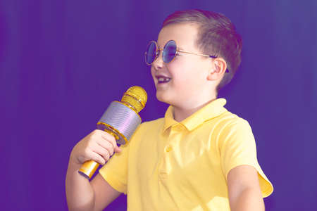 Close up image.The young boy kid child 9s old in yellow t shirt and blue eyeglasses is singing music on purple foggy toned illuminated stage.の写真素材