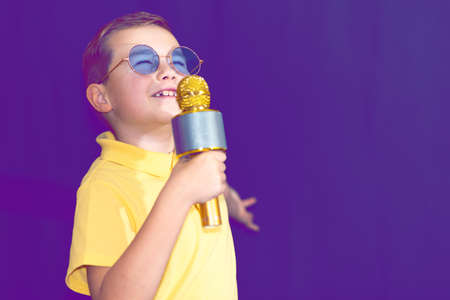 Close up image.The young boy kid child 9s old in yellow t shirt and blue eyeglasses is singing music on purple foggy toned illuminated stage.の写真素材