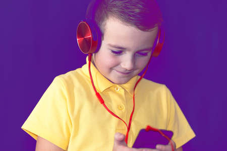 Close up of one young school boy using his phone and listening music alone or watching videos.Purple foggy toned background.の写真素材