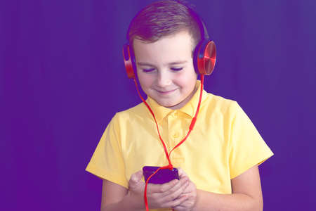Close up of one young school boy using his phone and listening music alone or watching videos.Purple foggy toned background.の写真素材
