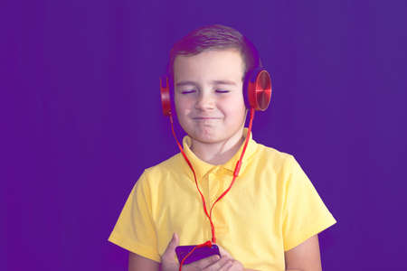 Close up of closed eyes young school boy using his phone and listening music alone or watching videos.Purple foggy toned background.の写真素材