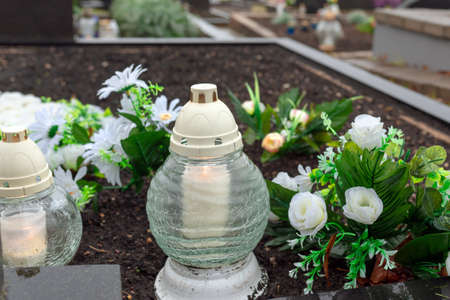 A candle and fake white roses at a cemetery.First november concept.At morning or evening