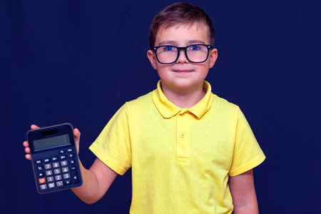 Close up Attractive young schoolboy with eyeglasses, yellow t-shirt holds a calculator.The...