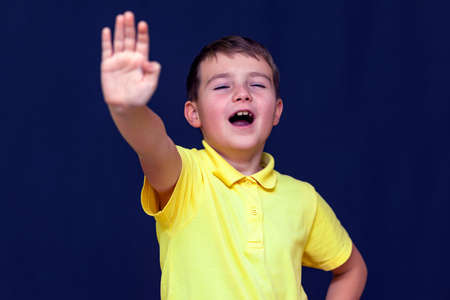 Young caucasian open mouth 9s boy putting his hand out making stop sign gesture.Blue studio background.の写真素材