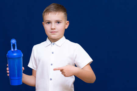 Portrait of happy little boy with water from plastic bottle on blue dark background Boy shows a bottle of plasticの写真素材