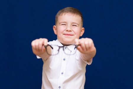 Portrait of a caucasian boy.He holds and shows glasses on dark blue background.He no longer wants to wear glasses.He is closed eyesの写真素材