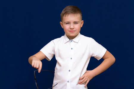 Portrait of a successful young caucasian boy.He holds and shows glasses on dark blue background.He no longer wants to wear glasses.の写真素材
