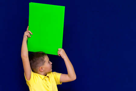 Side view Happy nice calm caucasian child boy holding a poster overhead for your information on the blue backgroundの写真素材