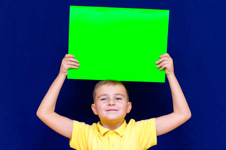 Happy nice calm caucasian child boy keep advertising above his head a poster for your information on the blue backgroundの写真素材