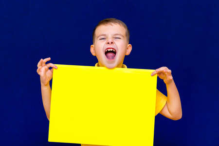 Portrait of joyful schoolboy posing with blank banner against studio blue background. Advertising concept.the boy shouts closed eyesの写真素材